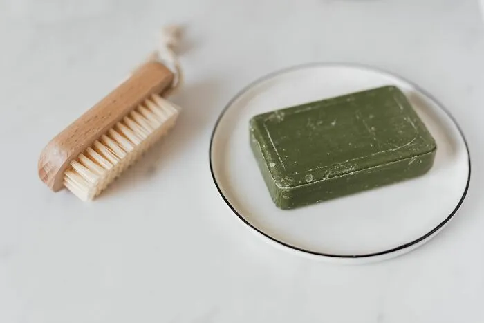 A green bar of soap on a dish next to a wooden brush, perfect for brilliant tips on sustainable living