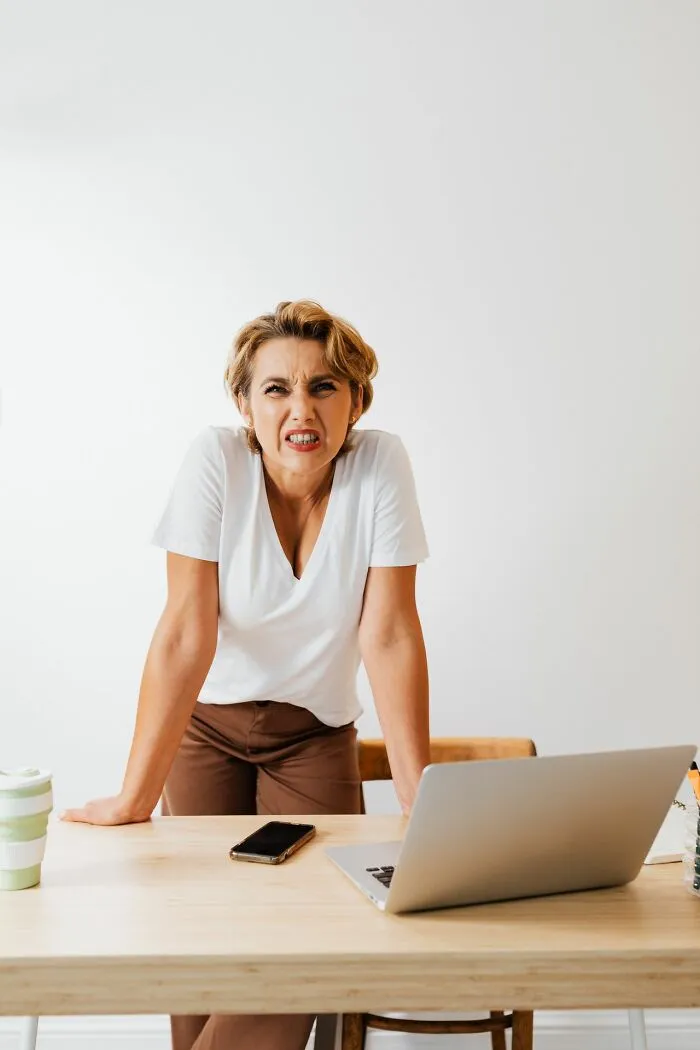 Frustrated woman expressing anger at desk with laptop and phone, depicting Karen behavior
