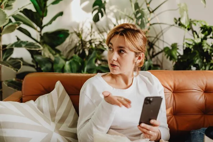 A confused woman on a couch looking at her phone, reflecting a moment when partners question their intelligence