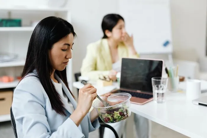 A woman sitting at her desk eating salad next to a laptop during lunch at one of people's jobs