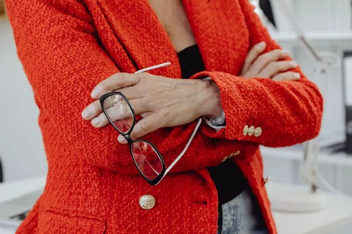 A woman in a red jacket holding eyeglasses with crossed arms, representing obvious lies.