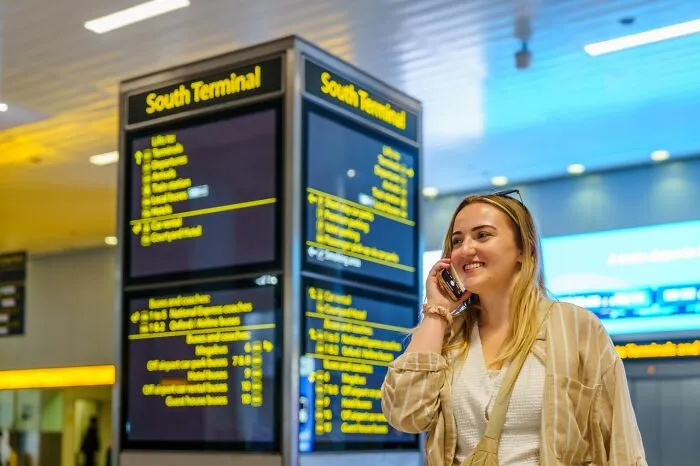 Smiling woman talking on phone at an airport terminal, using clever life tricks to navigate public transit.