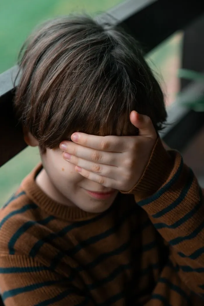Child covering face shyly in striped sweater with Karen stories theme