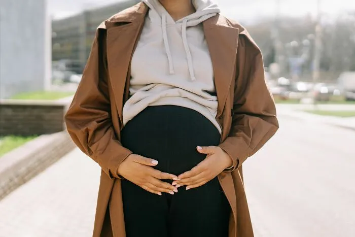 A pregnant woman wearing a brown trench coat holding her belly, related to real laws.