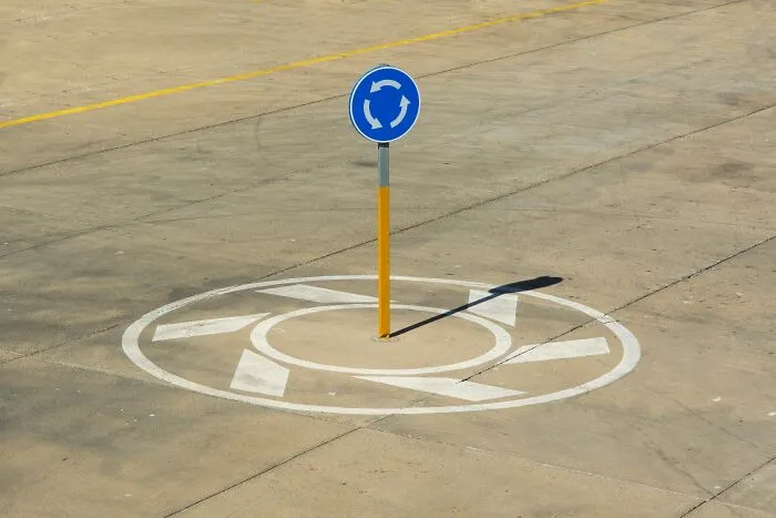 Blue roundabout sign painted on concrete in tiny communities with local news and drama