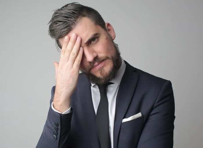 A man in a suit doing a facepalm after a costly mistake.