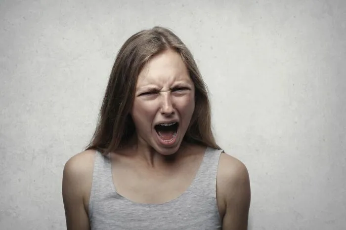 Young woman yelling with anger against neutral background