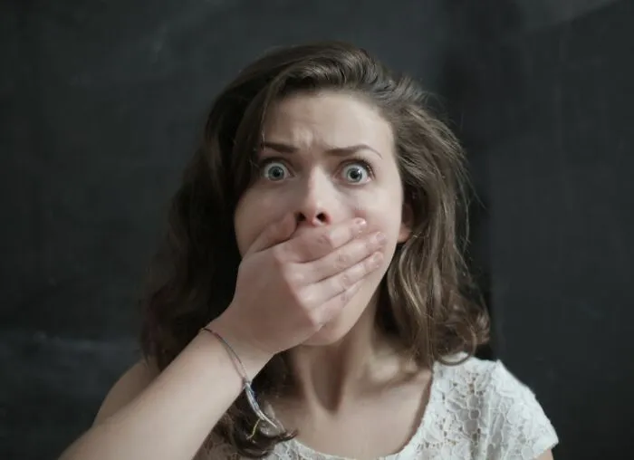 A young woman with wide, shocked eyes covering her mouth in fear, capturing an urgent feeling.