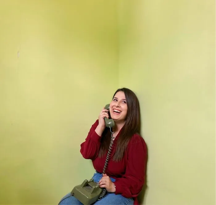 A woman smiling while talking on a vintage telephone, representing satisfying revenge stories.