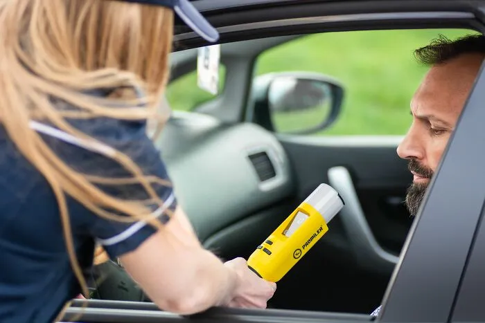 Police officer using a breathalyzer on a driver, demonstrating traffic laws and legal enforcement.