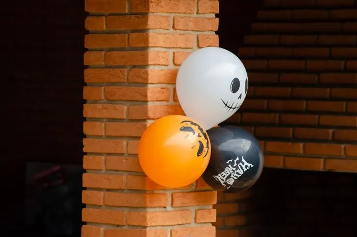 Spooky Halloween balloons with printed scary faces tied to a brick pillar for a Halloween party.