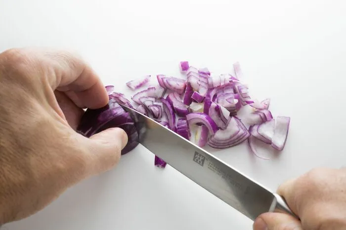 Hands chopping red onion into pieces with kitchen knife