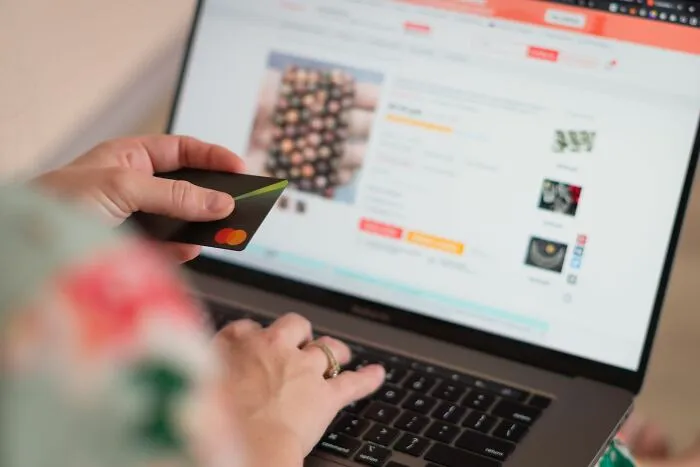A person holding a credit card while shopping on a laptop, displaying practical everyday life tips.