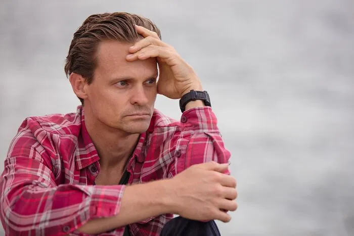 A man in a plaid shirt looking thoughtful and anxious as he keeps secrets.