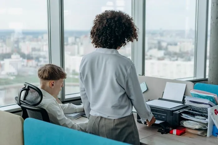 Two coworkers at a printer in an office, discussing things that made partners question their intelligence.