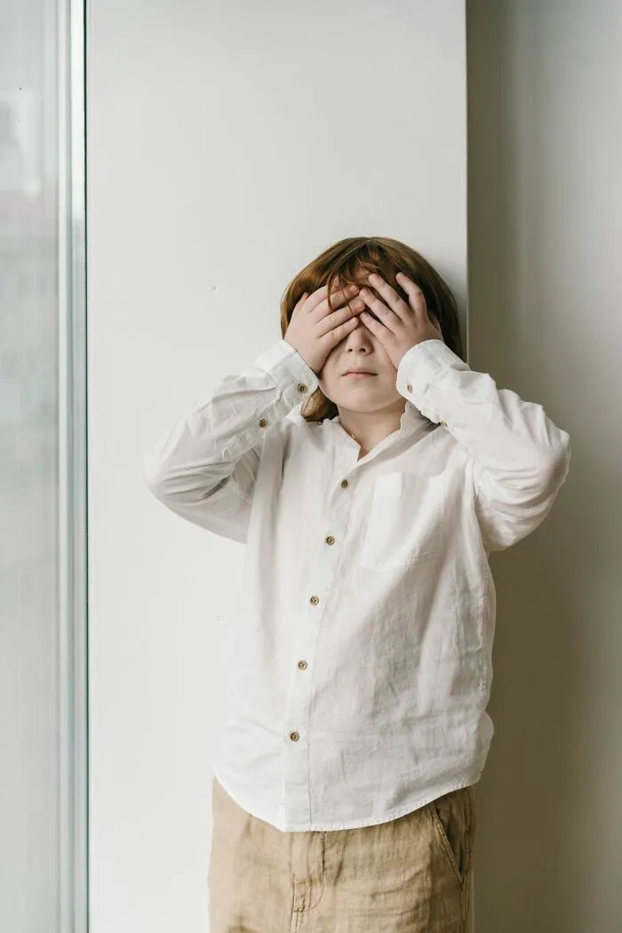 Child covering eyes in embarrassment representing kids growing up with Karens
