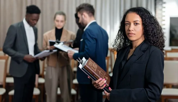 A woman holding a book titled The Law in front of colleagues, showcasing real legal concepts and loopholes.