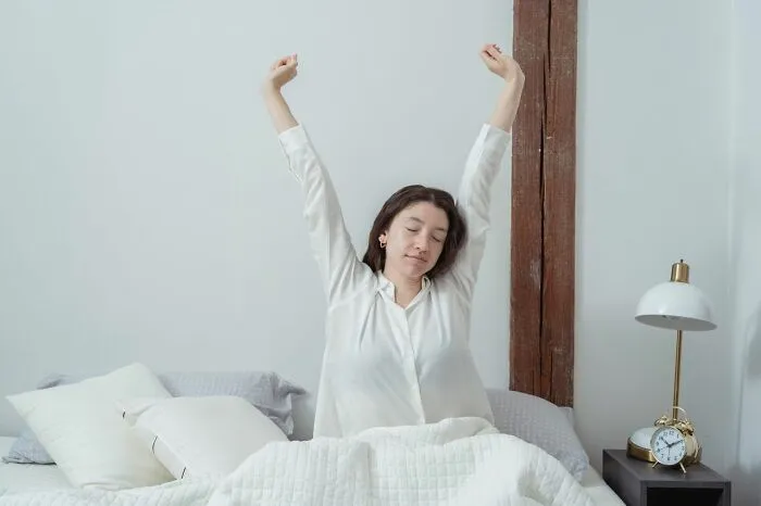 Woman stretching in bed after waking up, demonstrating simple life tricks for a better morning routine.