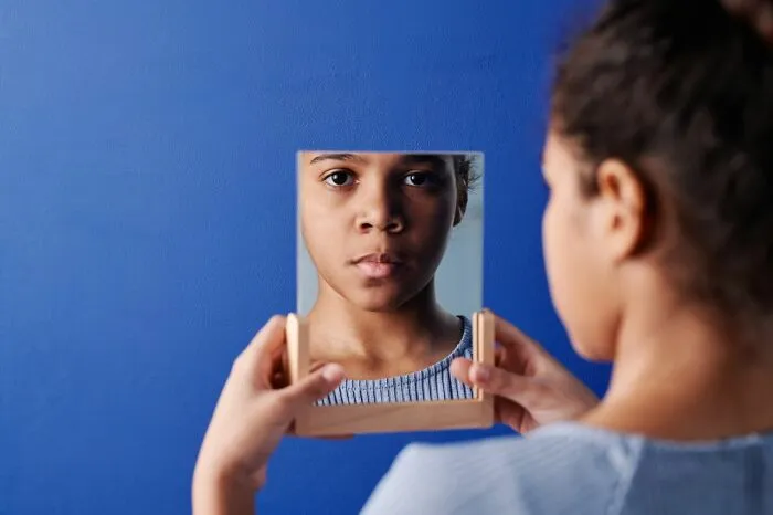 A young child looking into a small framed mirror instead of receiving trick-or-treating candy.