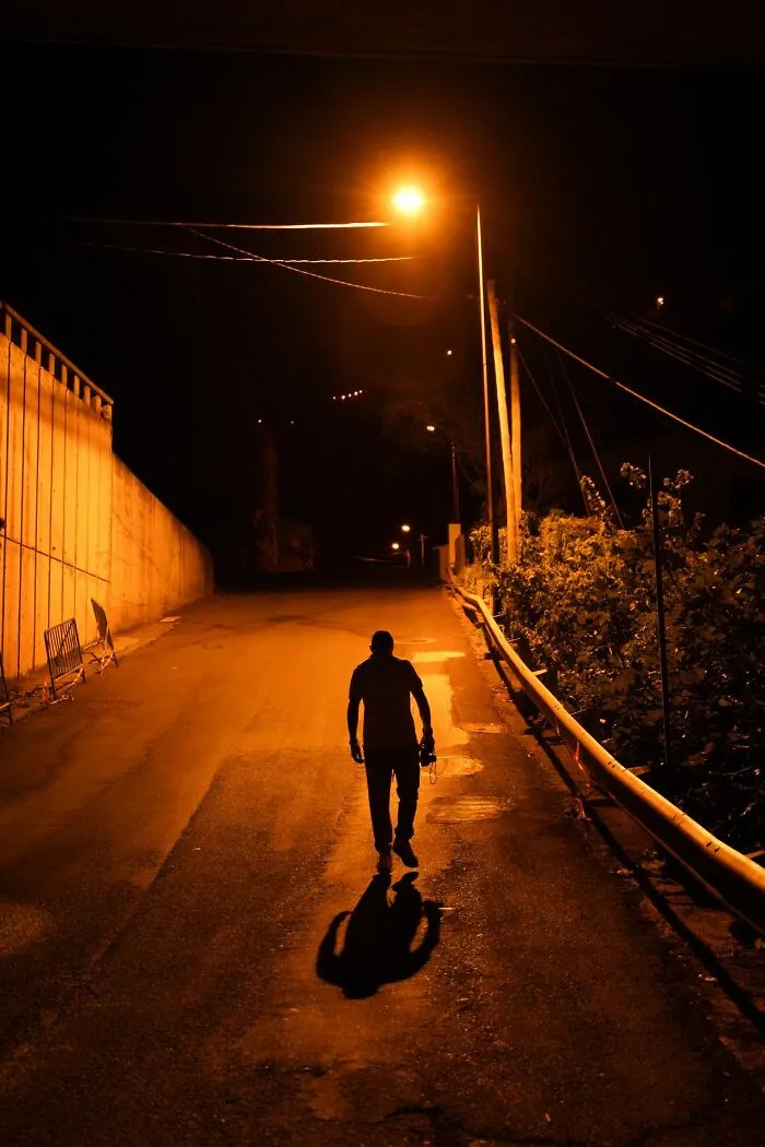 Silhouette of a person walking down a dark street at night, with an urgent feeling to leave