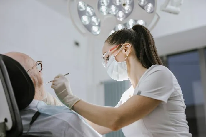 A female dentist wearing a mask and protective glasses treating an elderly patient, sharing health and life tips.