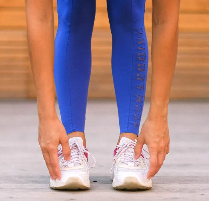 Person stretching in blue tech leggings and white sneakers