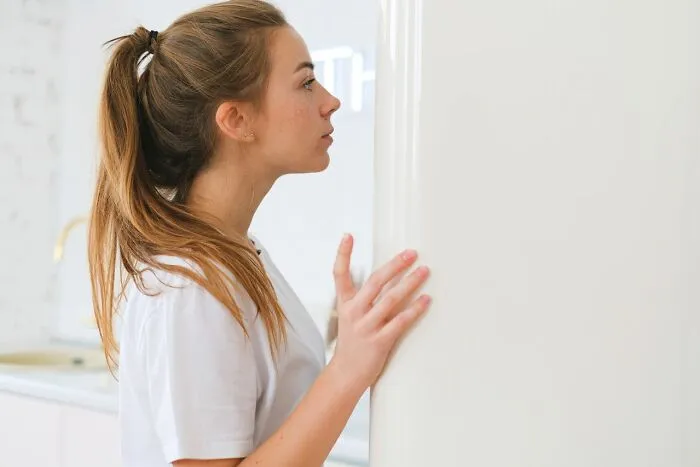 Young woman opening refrigerator door in kitchen