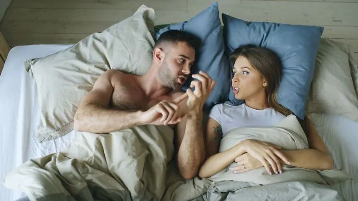 A man explaining something in bed to a skeptical woman, illustrating men wrong about women's bodies.