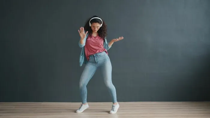 Woman wearing headphones happily dancing after reading about funny instances online.