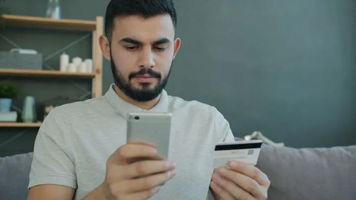 A man holding a credit card and smartphone looking at a massive bill