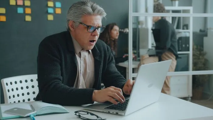 A businessman shocked by a costly single slip-up while looking at his laptop screen.