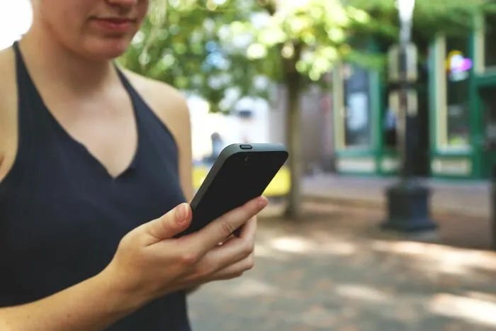 A woman holding a smartphone, representing unethical life pro tips on mobile apps.