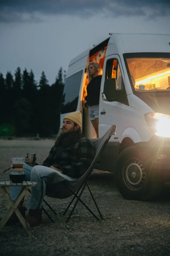 Man sitting outside camper van at dusk, a situation evoking an urgent feeling to leave immediately