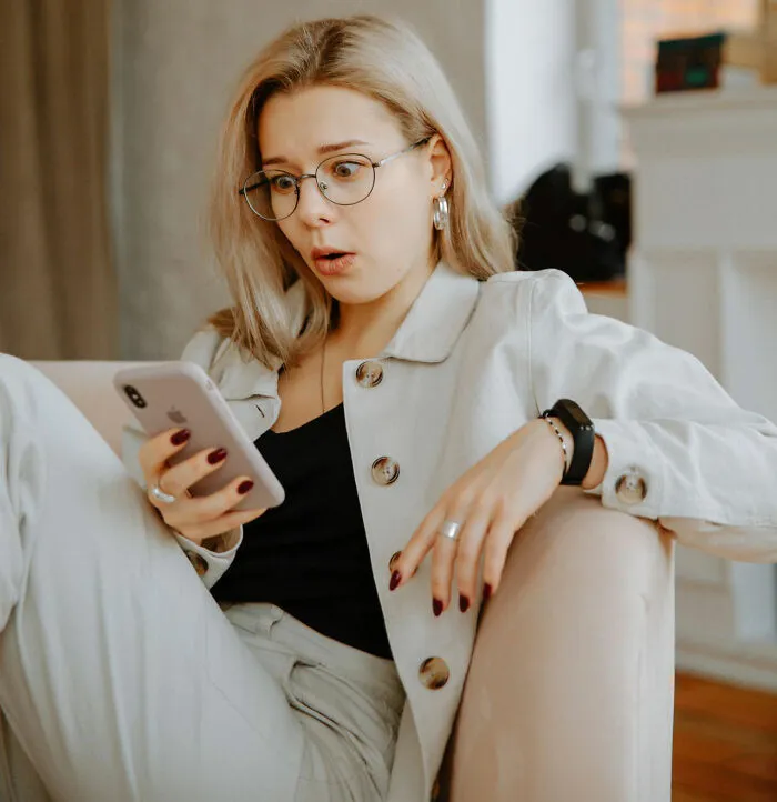 Blonde woman with glasses looking shocked at her smartphone, representing funny instances of awkward texts.