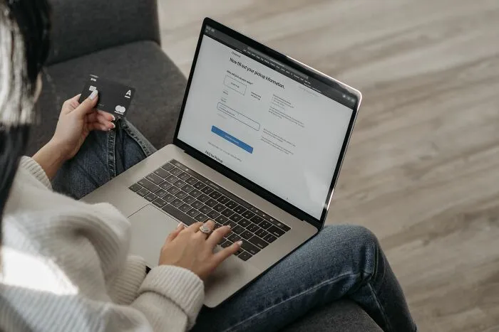 A woman holding a credit card while typing on her laptop, depicting unethical life pro tips for online shopping