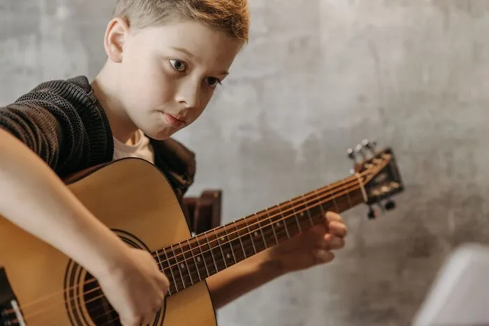 A young boy practicing an acoustic guitar, associated with obvious lies.