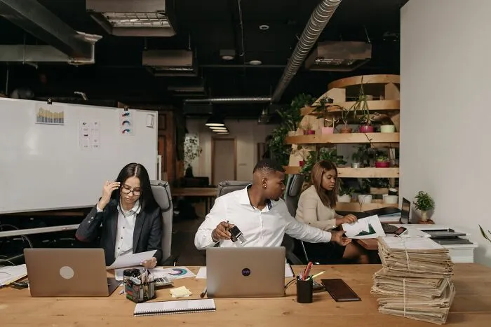 Office employees working diligently at a desk with laptops and paperwork, showcasing career and life tips.