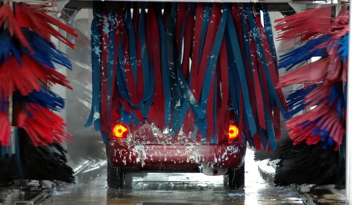 A red car going through an automatic car wash, reminding of a costly slip-up leading to a massive bill.