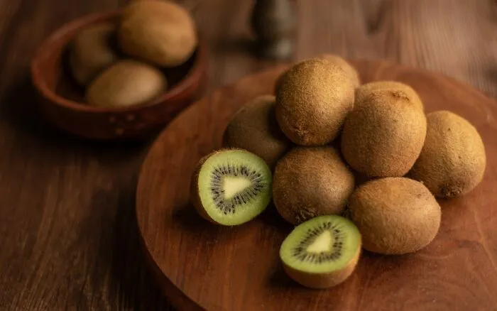 Fresh kiwifruit on wooden board with cut halves showing green flesh
