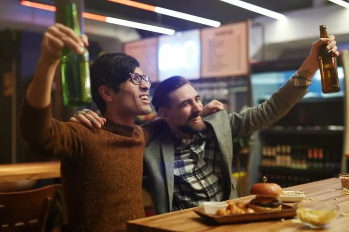Two men cheering with beers at a bar, unaware of any urgent feeling to leave immediately