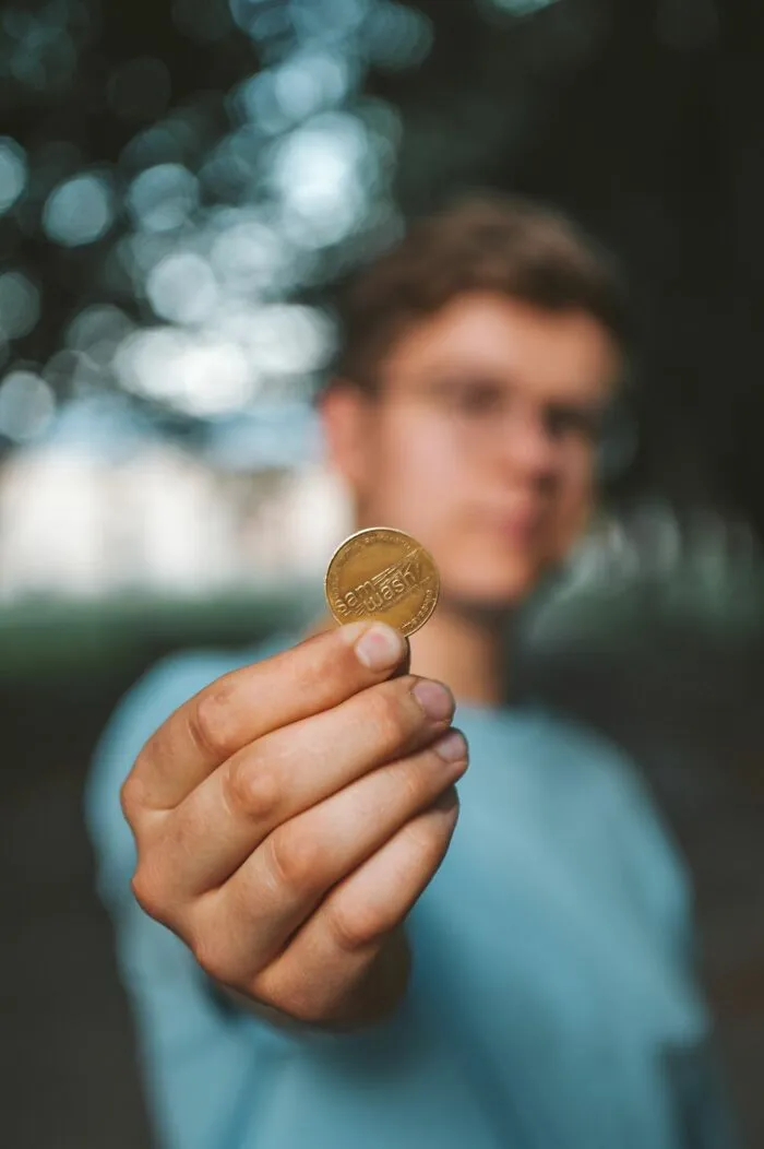 A hand holding up a metallic coin token instead of candy while trick-or-treating