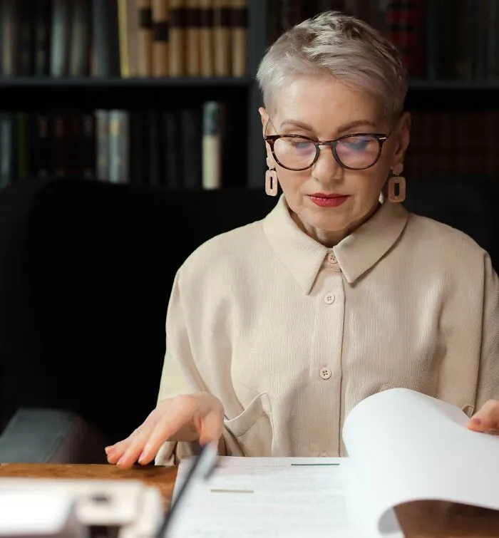 Focused mature woman reviewing legal documents, studying complex laws and loopholes