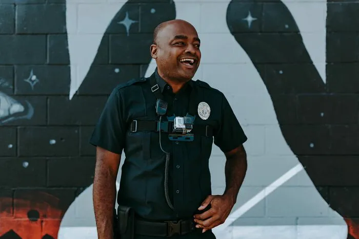 Police officer wearing body camera standing in front of mural and smiling