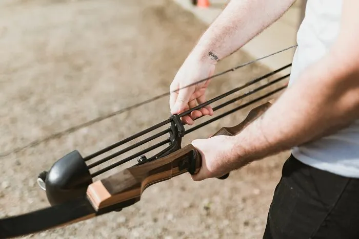 Person holding a wooden bow with arrows examining sports and activity loopholes