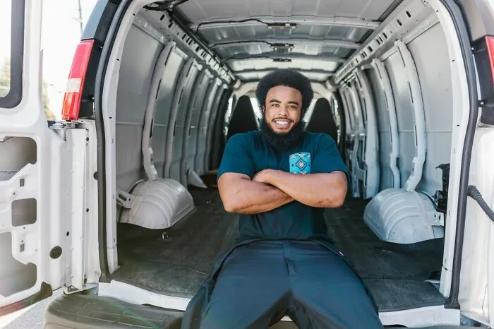 A smiling man sitting in the back of an empty white moving van, ready to leave immediately.