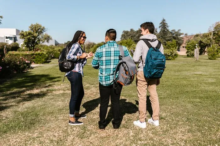 Three students with backpacks walking on campus, depicting unethical life pro tips for college.