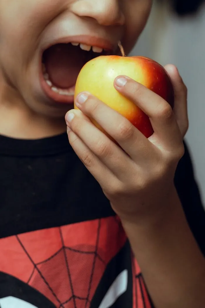 A child opening wide to bite into a fresh apple instead of receiving candy while trick-or-treating.