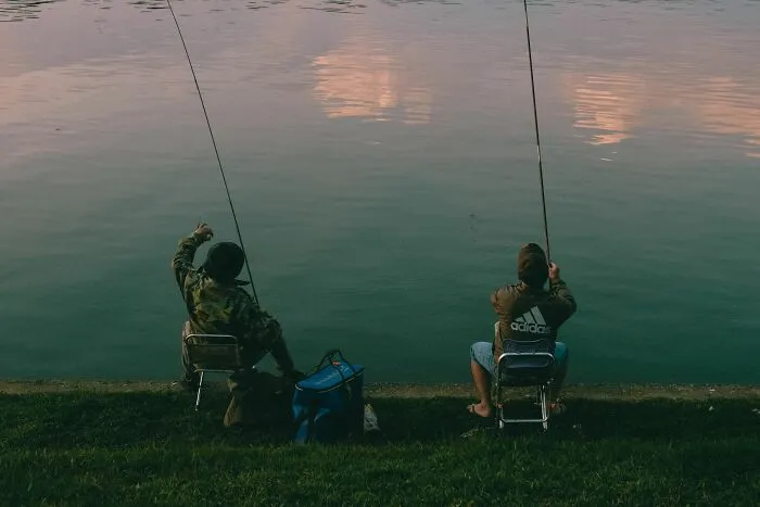 Two people sitting on folding chairs and fishing by a calm lake, trusting their gut feeling.