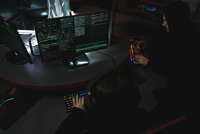 Two computer programmers working in a dark room with multiple monitors