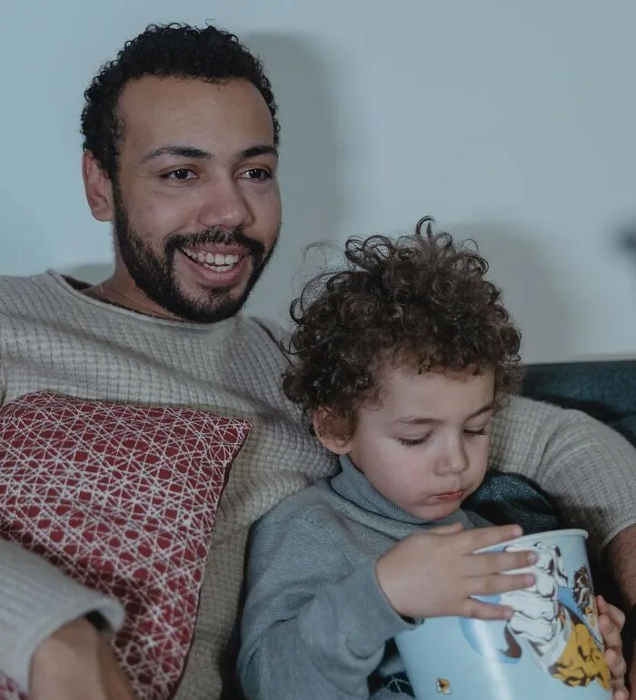 A father and young child eating popcorn together on the couch, related to real home and family laws.